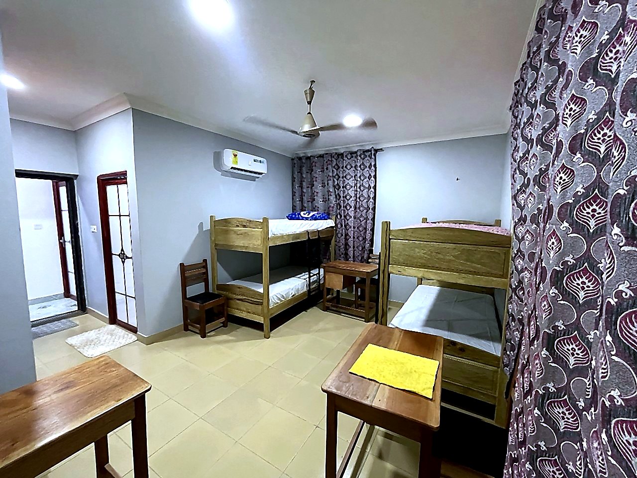 Three-bed hostel room with study desk, air conditioning, wardrobe, and TV